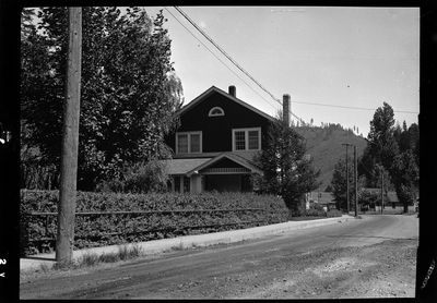 Photo of a home in Wallace, Idaho taken for Household Magazine. The house is mostly obscured by a line of bushes and trees, but you can make out that the house is two stories tall.