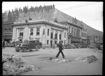 Photo of downtown Wallace, Idaho taken for Household Magazine. The J. C. Penney Company store is easily visible, along with other businesses. Several people are walking on the sidewalks, and cars can be seen both driving on the streets and parked on it.
