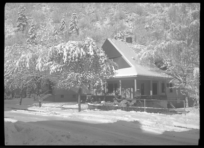Photo of the Gyde home in the snow. The roof, ground, and surrounding trees all have a heavy layer of snow covering them. The house is mostly obscured by trees.