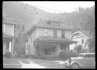 Photo of the Seelig house that has a car parked on the side of the street in front of it. The house is two stories tall and has large trees in the front yard.