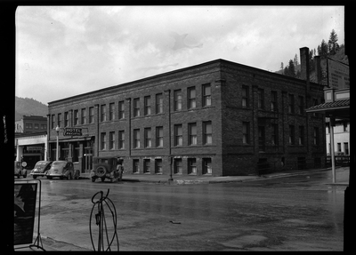 Photo of the Pacific Hotel (which sign reads "Hotel Pacific") building. There are several cars parked on the side of the road in front of it.