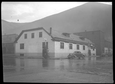 Photo of the exterior of the Wallace Bowling Alley in Wallace, Idaho. There is a car parked on the side of the road next to the building. The street appears to be flooded.