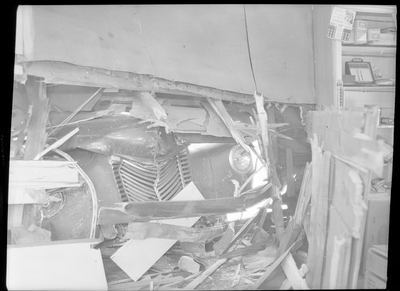 Photo of a truck that was crashed into the side of the General Food Store, taken from the interior of the building. The front and hood of the truck are visible through the hole in the wall, and debris from the impact is all around the room.