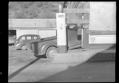 Photo of a truck that was crashed into the side of the General Food Store, damaging the wall and a sign on the exterior. Photo taken from the side, which causes most of the damage to be obstructed by a gasoline pump and a wall.