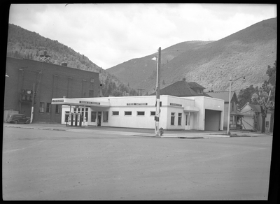 Photo of the Union Oil Dealer building. Along the exterior wall of the building there are several signs. Above the gasoline pumps are two signs, "TM.-Tex-Elliston," and "Union Oil Dealer," and on the last stretch of wall reads, "Tires; Batteries." Another garage in the building is visible on another wall.