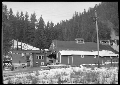 Photo of the side of the exterior of the Wallace Meat Company building. There is a house blocking part of the view with several cars parked outside. There is also snow on the ground.