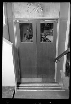 Photo of the stairs that lead down to the doors of the Hotel Pacific Cafe. On the window of the door is a decal reading "Week days 5am-11pm; Saturday 6am-9pm; Sunday." There is also a sign above the door that reads "Cafe."