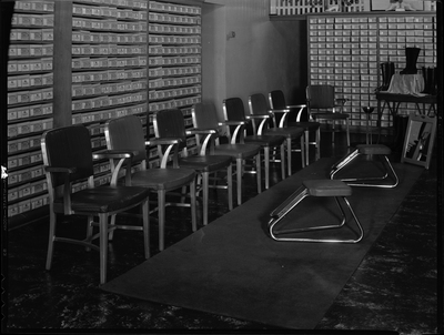 Interior photo of Murphy Clo Company Bootery. There are shoes on display and shoe boxes line the shelves on the walls. There is a small area with chairs in the middle of the room for people to try on shoes.