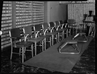 Interior photo of Murphy Clo Company Bootery. There are shoes on display and shoe boxes line the shelves on the walls. There is a small area with chairs in the middle of the room for people to try on shoes.