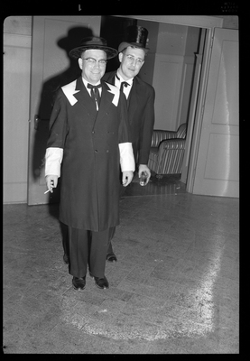 Two men standing together at a Rotary Club party. They are formally dressed and smiling at the camera. One man is holding a drink and the other is holding a cigarette.