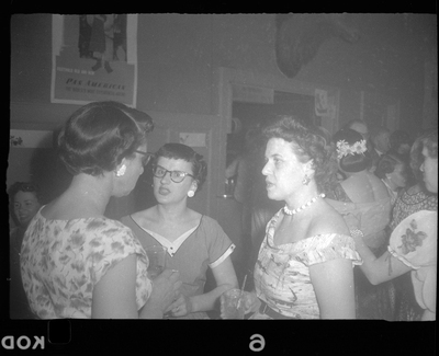 Three women at Rotary Party talking together. One woman has her back to the camera, and another is looking at the camera. They are holding drinks and wearing nice dresses.