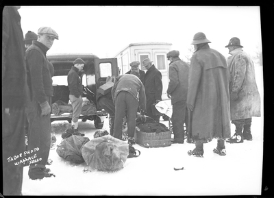 A group of people are standing in the snow near two cars, one with the back doors open, preparing to load what is presumably dead bodies into it. They are responding to an avalanche hitting a train. Three people died.