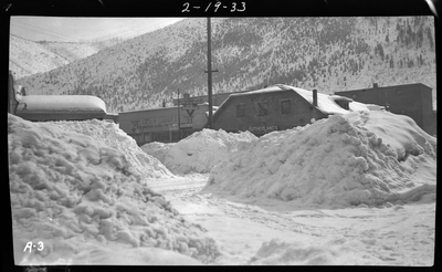 Photo of the Sutherland's building and a few others in the snow. There are large piles of snow between the photographer and the buildings which obscure most of the buildings.