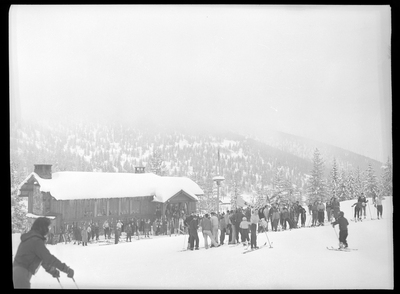 A large group of people in ski gear are gathered together outside at Lookout Pass. The ground and the building that everyone is gathered around is covered in snow, and trees can be seen in the background.