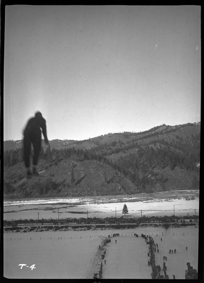 An unidentified person is mid jump at a ski jump event at Lookout Pass. There is snow on the ground and a crowd of people watching.