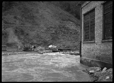 Photo of what appears to be a flood in a residential area. The water reaches up to the side of the building, possibly the Idaho Ski Club Lodge building, and across the water there are several cars parked on the ground.
