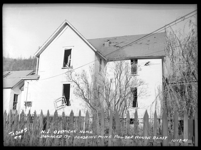 Exterior damage to N. J. Osborne's home after the Sunshine Mine powderhouse explosion. There is visible damage to the windows and roof, as well as a hole in the wall of the house where a rock broke through.