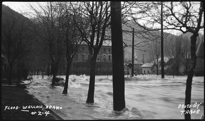 The ongoing flood in Wallace, Idaho. The water is rushing through a residential area, covering the streets and rushing against houses.