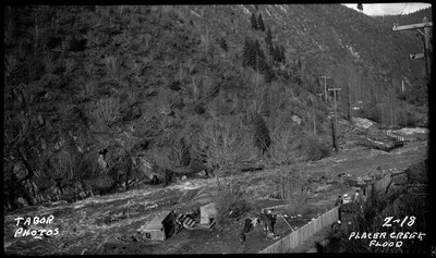 Image of the damage caused by flooding at Placer Creek. People can be seen near a fence by the rushing water.