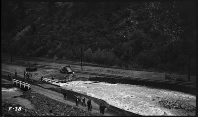 Overhead image of road damage caused by flooding. People can be seen standing near the floodwaters.