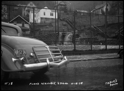 Two people in the distance watching water rushing through stacked logs. A car can be seen on the right.