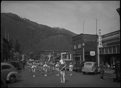 Band members, a few women and mostly men, in the Benevolent and Protective Order of Elks parade. Spectators are watching near the cars parked on the street.