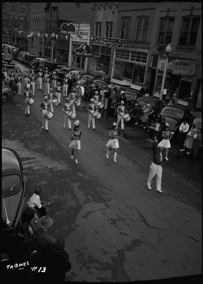 Wallace High School band in the Elks Roundup parade. Spectators watch from the sidewalk and by the cars parked along the street.