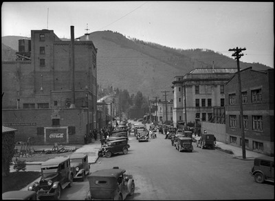 View of the street during the opening scenes of the Sunset Mercantile parade. Cars are parked along the street.