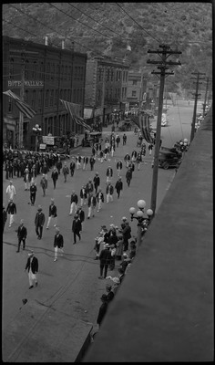 Men walking in the Benevolent and Protective Order of the Elks parade. They are wearing hats with fake antlers. Spectators watch from the side of the street. Garlands hang across the street.