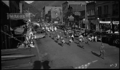 Marching band and other people walking down the street during the V.F.W. State Convention parade. Spectators are watching from the sidewalk.