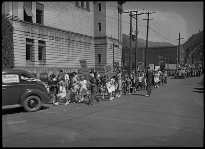 Children walking in the street during a back-to-school parade, some are holding signs.