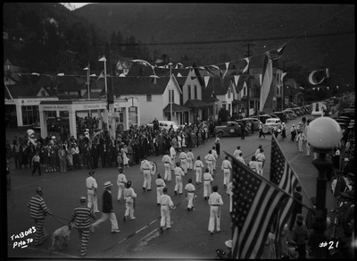 View of marching band from the back during the Benevolent and Protective Order of Elks roundup parade. Crowds of spectators watch along the sides of the street,