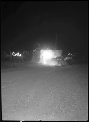 A group of people standing in the dark near a bright light, possibly the beginning of the motorcycle hill climb.