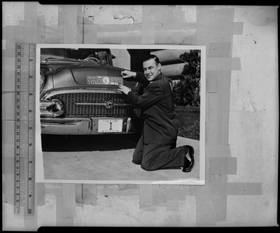 Photograph of a man putting on a sticker that reads, "Wallace Idaho Silver Jubilee June 11-15 1938." There is a ruler next to the photograph.