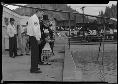 A man wearing a hat helps a child hold a long pole over a pool during the Silver Jubilee fire derby event and art fair.