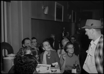 People sitting at a table and talking during the Albie's March of Dimes event. A man wearing a hat is seen standing on the right speaking to the seated people.
