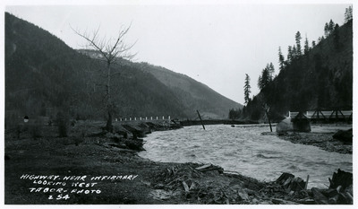 Floodwaters approach a highway near an infirmary, looking west. There is a bridge and some minor debris visible in the photo.