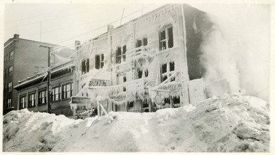 Soot and what appear to be icicles and frost cling to the structure of the Ryan Hotel after a fire. There appear to be no window panes anymore, and there are piles of snow and soot on the ground.