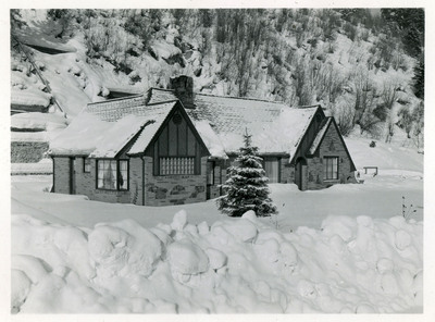 Snow covers a building, trees, and a nearby hillside.