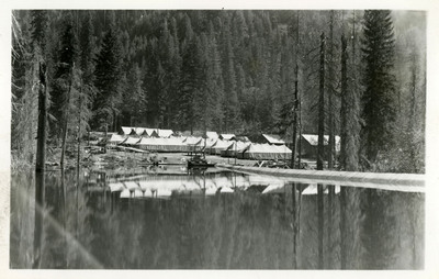 View of a few buildings near a lake. Trees in the background.