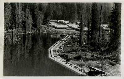 View of a few buildings near a lake. Trees in the background.