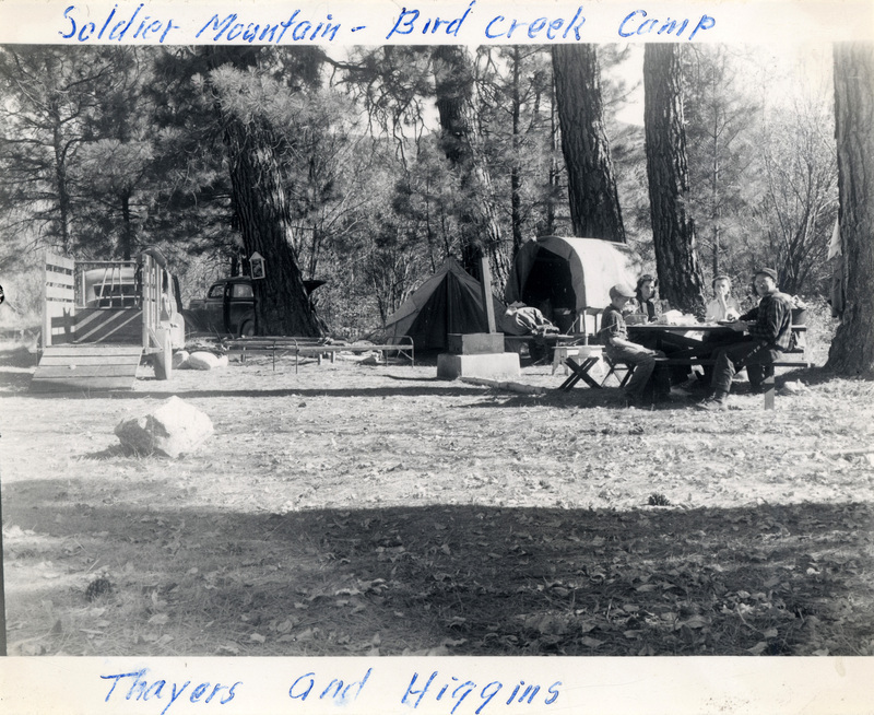Four people eat together at a picnic table next to a campsite. The photo reads: 'Soldier Mountain - Bird Creek Camp. Thayers and Higgins." The number 213 is stamped on the back of the photograph.