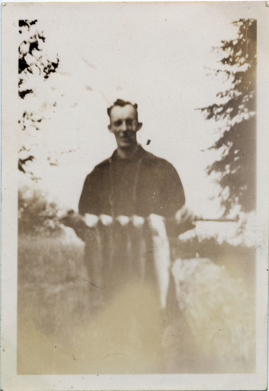 A man holds five fish which have been skewered through the head with a stick. The number 51 is stamped on the back of the photograph.