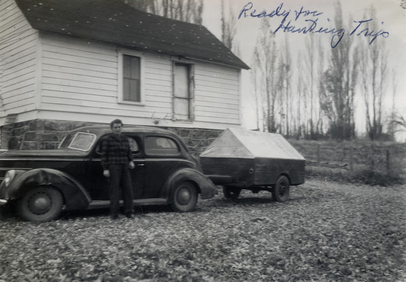 A person stands in front of a car with a camping trailer hitched to it, in front of a house. The picture is captioned: "Ready for Hunting Trip." The back of the photo is stamped with a number 4, with following numbers cut off.