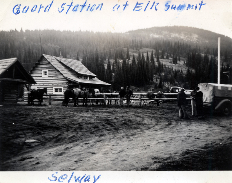 People and horses stand near a fence in front of a small building. The photo is captioned: "Guard Station at Elk Summit Selway." The back of the photograph is stamped with the number 188 and "Printed by The Camera Shop Sun Valley, Idaho Oct 15 1942."