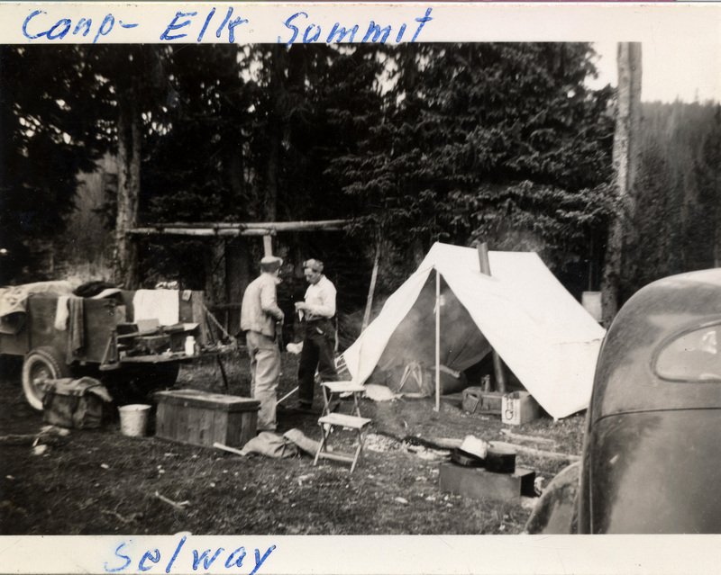 Two people stand in front of a tent. An automobile and camping trailer are in the background. The photo is captioned "Camp - Elk Summit Selway." The back of the photograph is stamped with the number 188 and "Printed by The Camera Shop Sun Valley, Idaho Oct 15 1942."