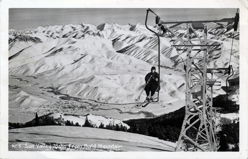 A postcard with an image of a person riding a ski lift on the front side. Printed on the bottom of the picture is: "KC-5 Sun Valley, Idaho, from Bald Mountain." The back side of the postcard is blank.