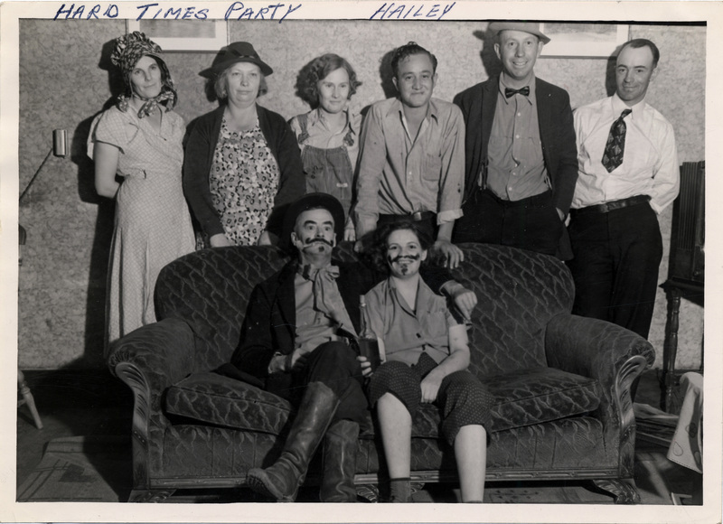 Two people sit on a sofa, and six people pose behind it. They are dressed in depression-era clothing, and some people have drawn-on facial hair. "Hard Times Party Hailey" is written on the front of the photograph.