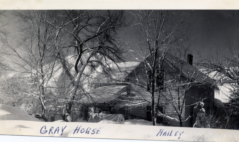 A house is surrounded by bare trees and covered in snow. "Gray house Hailey" is written on the front of the photograph.