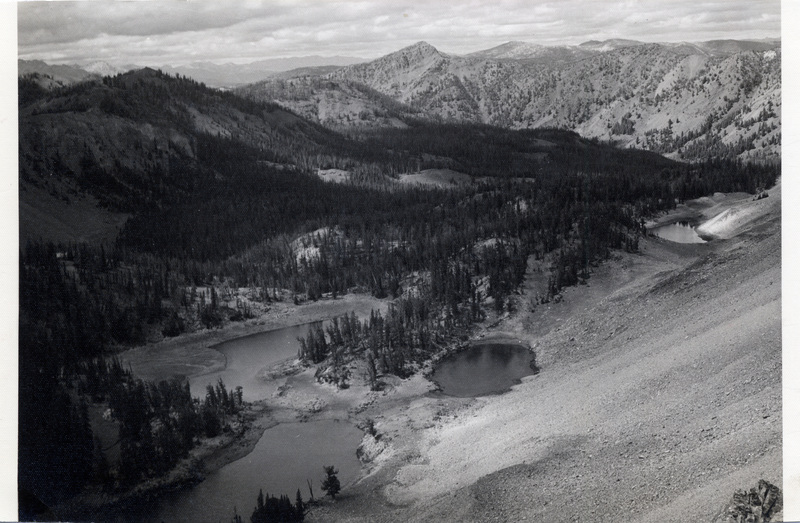 A body of water at the base of a mountain range, surrounded by pine trees.